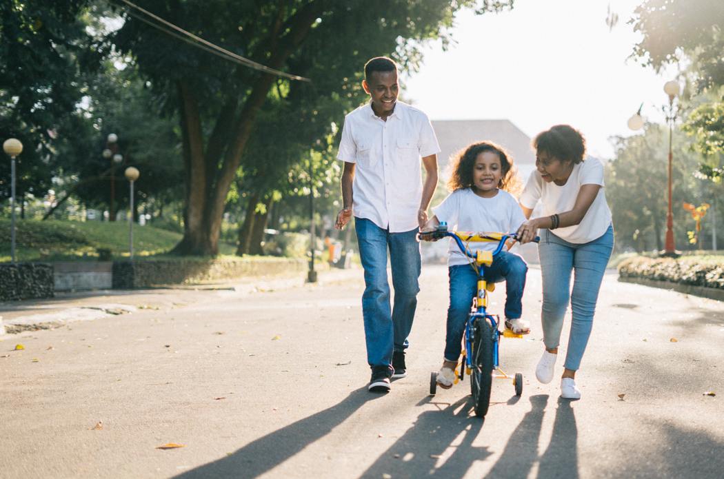 mom and dad teaching a little girl to ride a bike